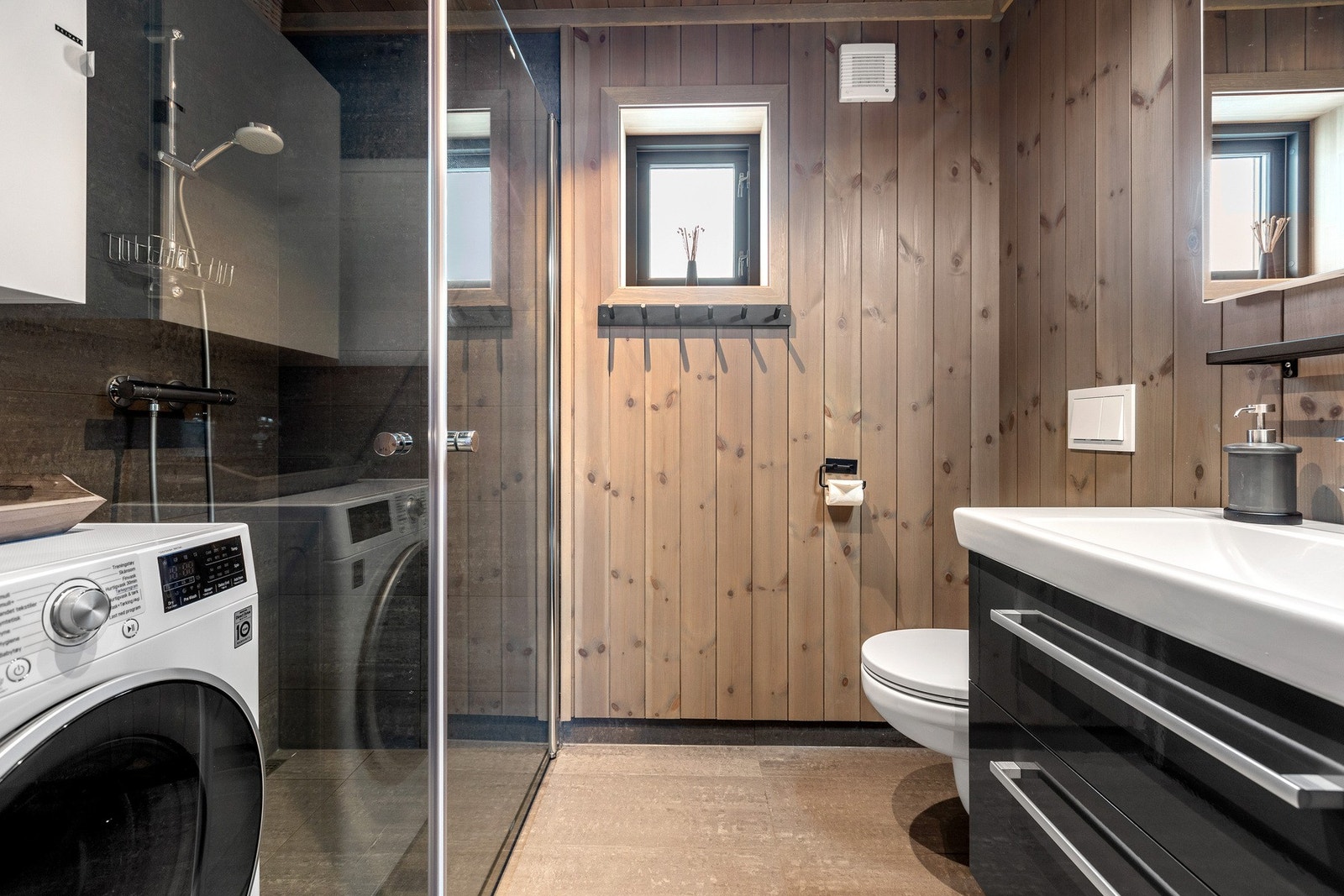 Badet har et moderne og helhetlig uttrykk med 30 x 60 cm fliser på gulvet, varmekabler og trepanel på veggene. Galleribilde
