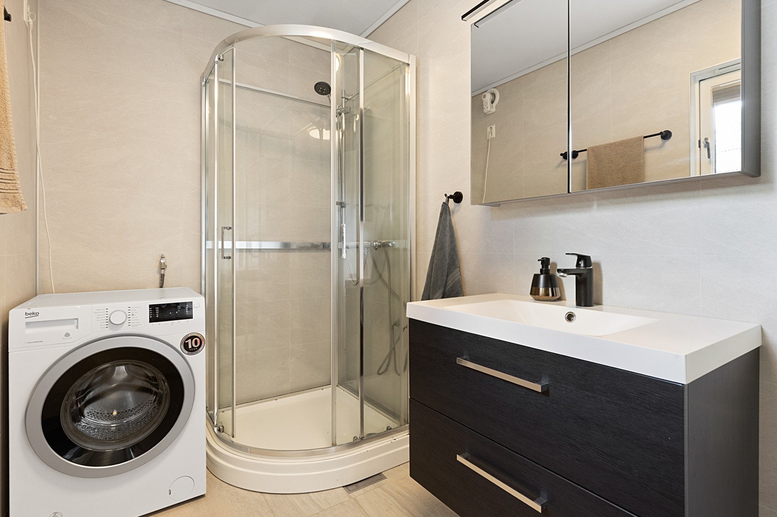Badet er innredet med wc, servant med innredning, speilskap, dusjkabinett og opplegg for vaskemaskin. Galleribilde