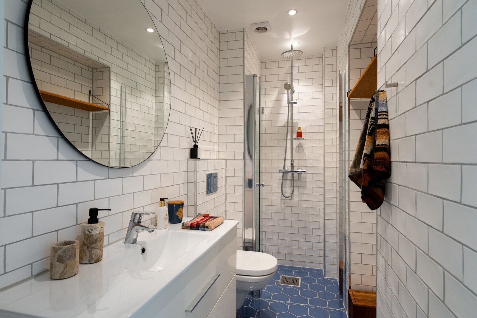 Badet viderefører boligens lyse og klassiske uttrykk, med en rolig og harmonisk atmosfære, med delikate, blå heksagonfliser på gulv med behagelig gulvvarme og tidløse, hvite veggfliser. Galleribilde