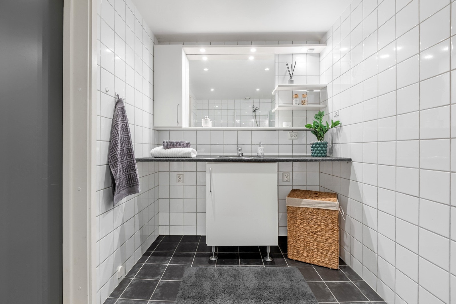 Badet er holdt i et tidløst uttrykk med hvite veggfliser og mørke gulvfliser. Opplegg for vaskemaskin. Galleribilde