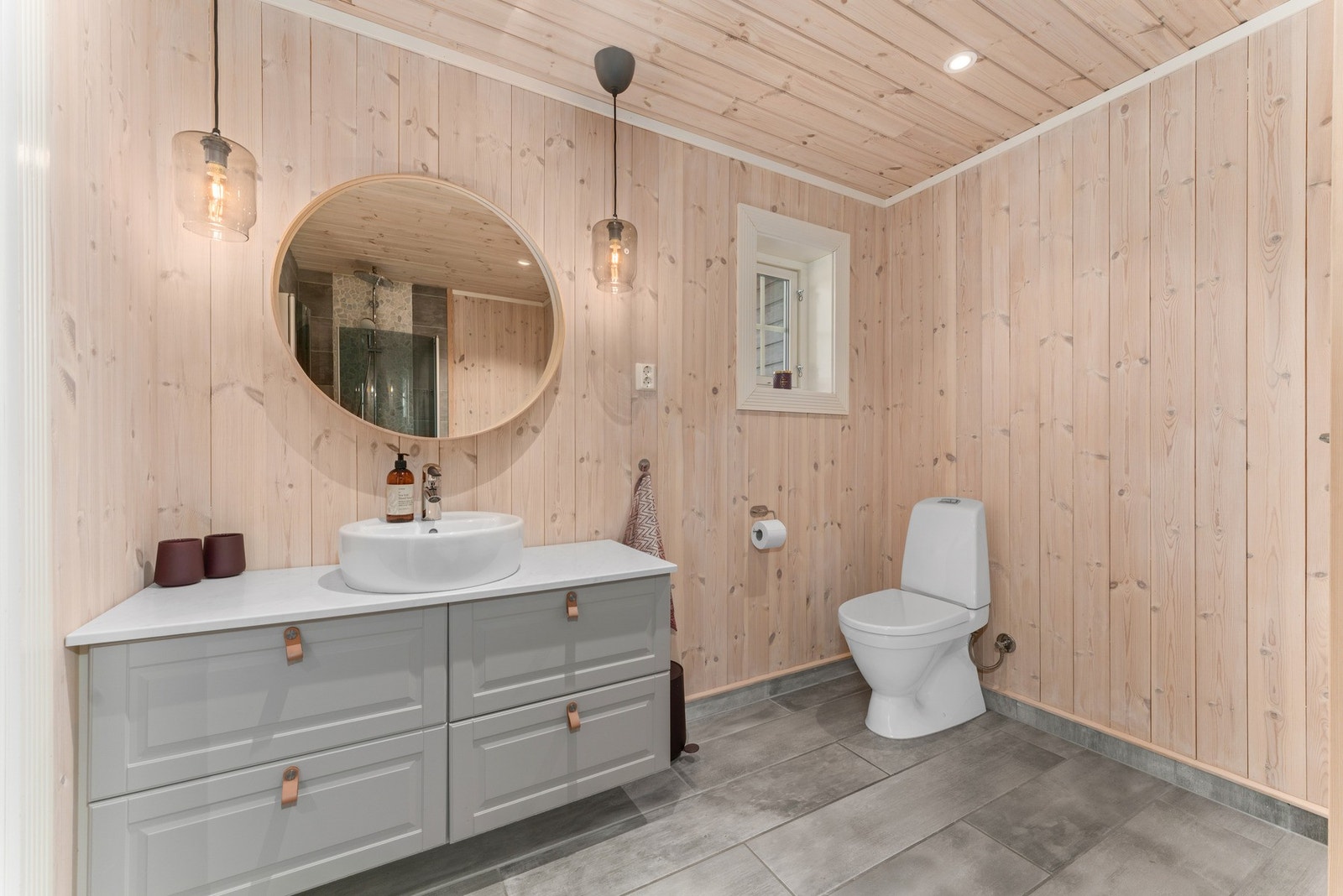 Badet er fra 2017 og har en lun utførelse med trepanel på vegger og i himlingen, kombinert med grå gulvfliser og flislagte overflater i dusjsonen. Galleribilde
