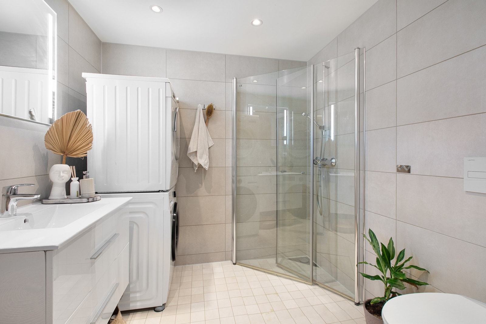 Badet har flislagte vegger, flislagt gulv med gulvvarme. Vegghengt servant, dusjhjørne med dører og vegghengt toalett Galleribilde