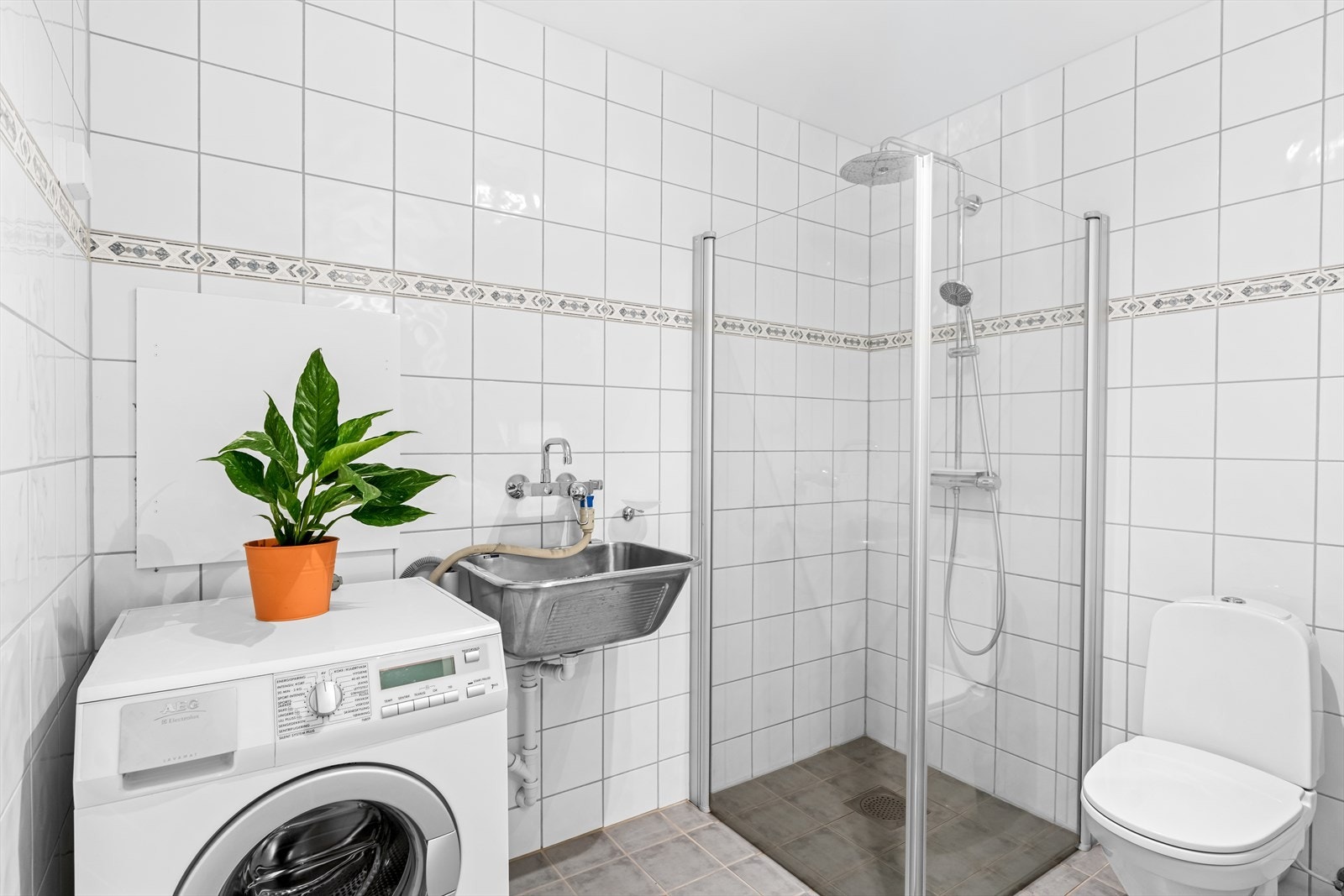 Badet er innredet med skap med profilerte fronter, servant, gulvstående klosett, dusj på gulv og opplegg for vaskemaskin. I tillegg har rommet mekanisk avtrekk. Galleribilde