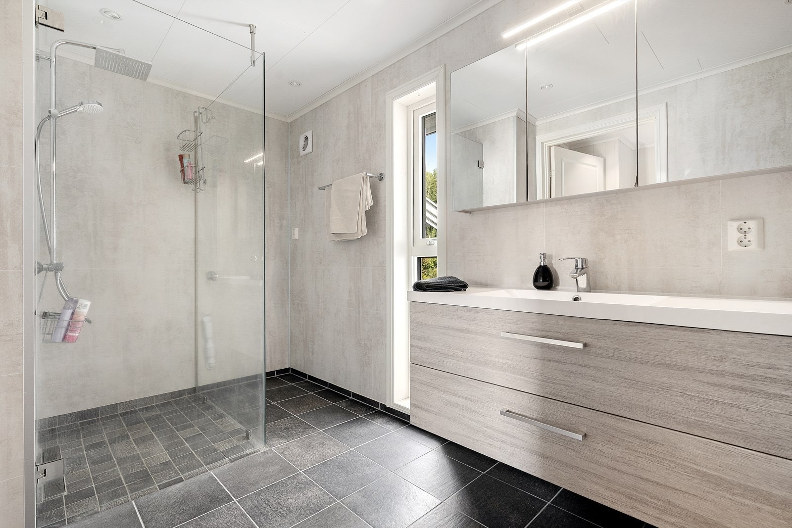 Badet er innredet med nedfelt servant, veggmontert toalett, dusjvegger og opplegg for vaskemaskin. Galleribilde