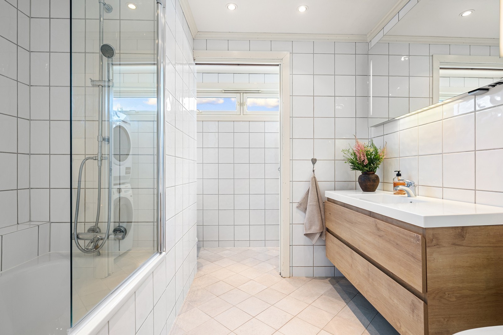 Badet er innredet med servant, speil med integrert belysning, veggmontert toalett og innebygget badekar med dusj Galleribilde