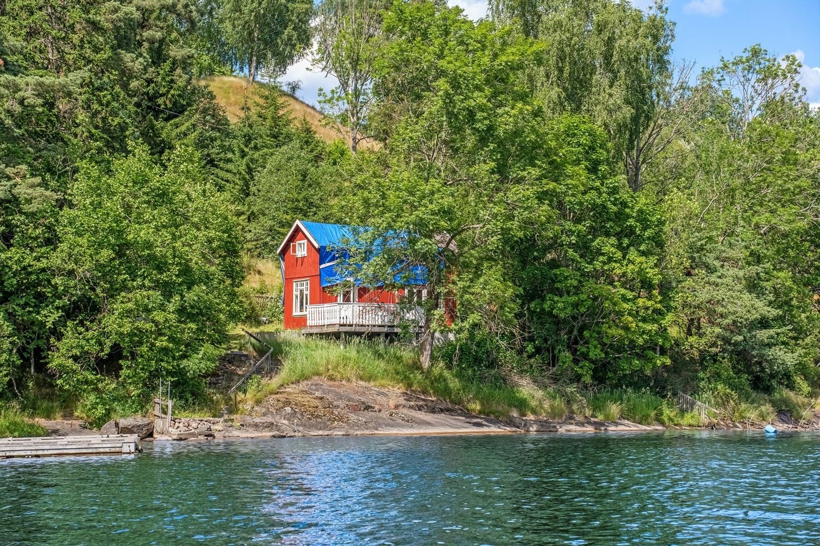 En liten og sjarmerende hytte med en beliggenhet det er vanskelig å ikke bli glad i. Her ligger vannet helt inntil terrassen, så nært at morgenbadet nærmest begynner med ett skritt fra hyttedøren. Galleribilde