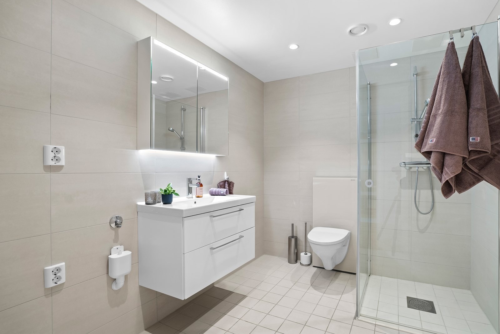 Badet har et moderne og tidløst uttrykk med lyse fliser og god belysning. Galleribilde