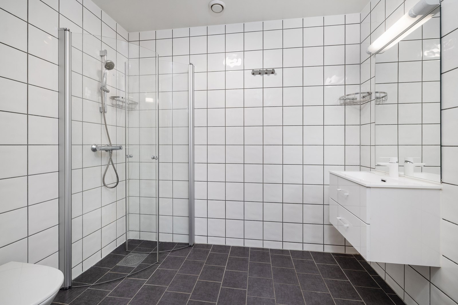 Romslig bad med lyse fliser på veggene og mørkere fliser på gulvet. Galleribilde