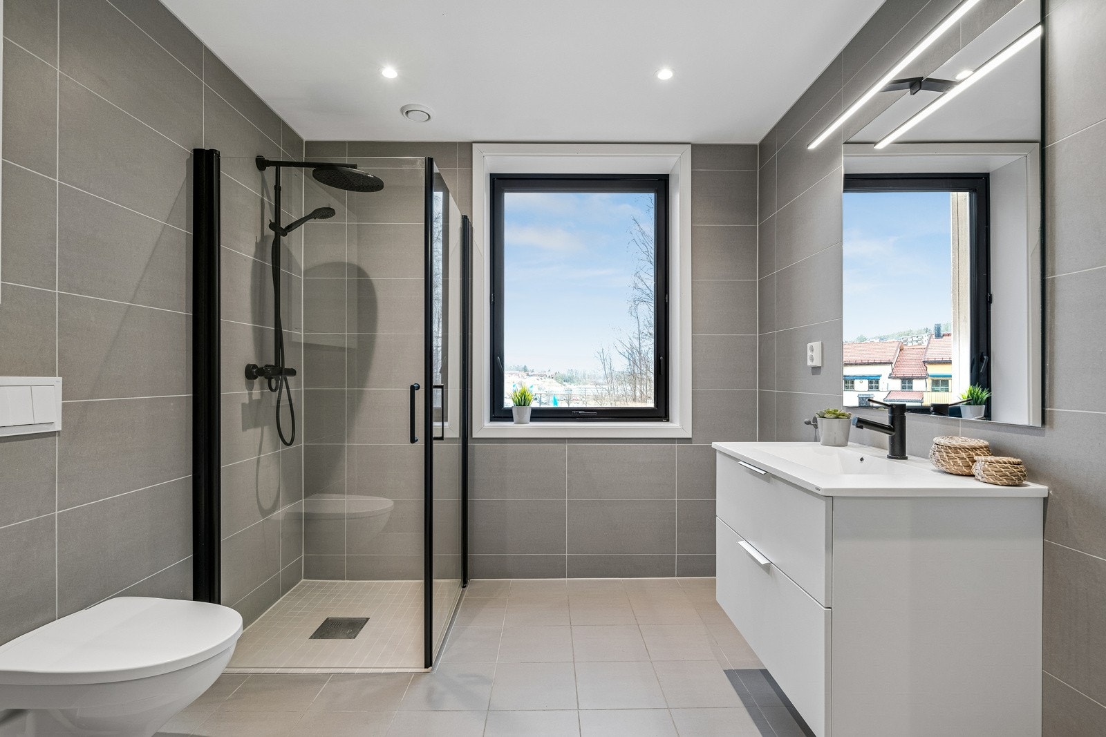 Stort, pent bad med stilrene og tidsriktige fliser på gulv på vegger. Badet har servant innredning som har godt med skapplass, vegghengt wc og dusjhjørne med vegger av herdet glass. Galleribilde