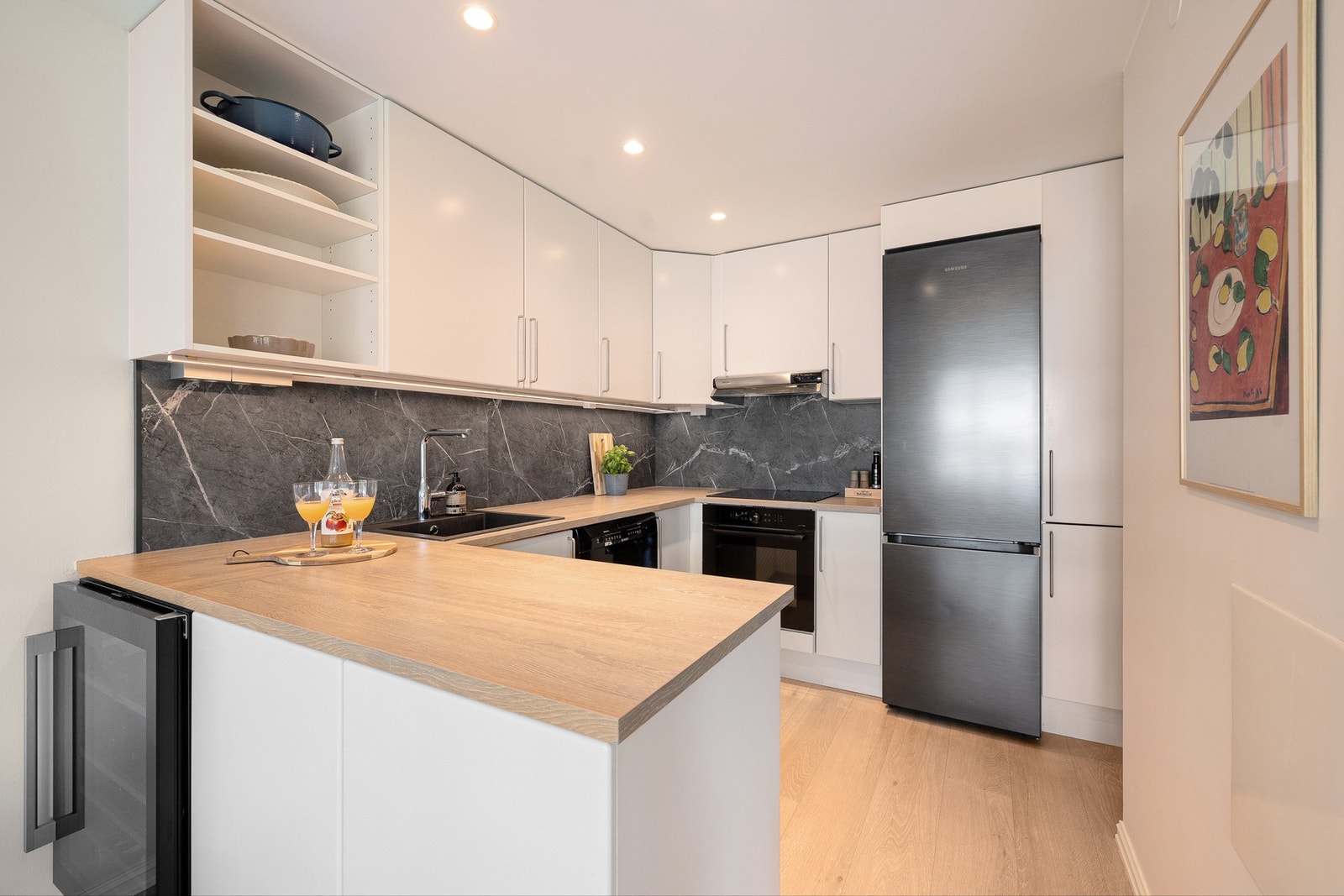 Stilren innredning fra Sigdal med hvite glatte fronter og pen benkeplate i eik laminat med marmoret kitchenboard over. Galleribilde