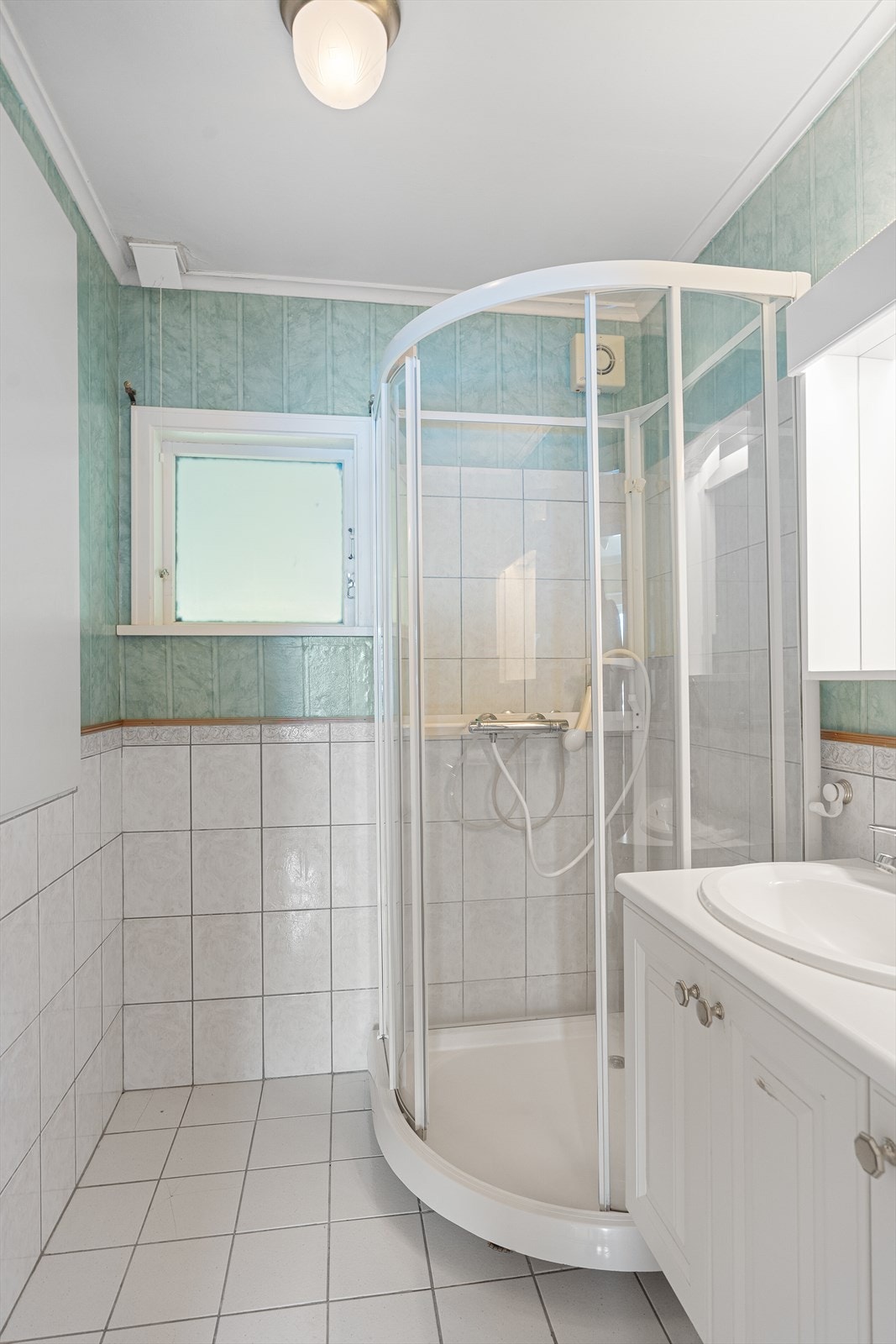 Badet er innredet med baderomsinnredning med nedfelt servant, dusjkabinett og gulvmontert toalett. Gulvet er flislagt, veggene har tapet og flis, og himlingen har malt strekkpapp. Galleribilde