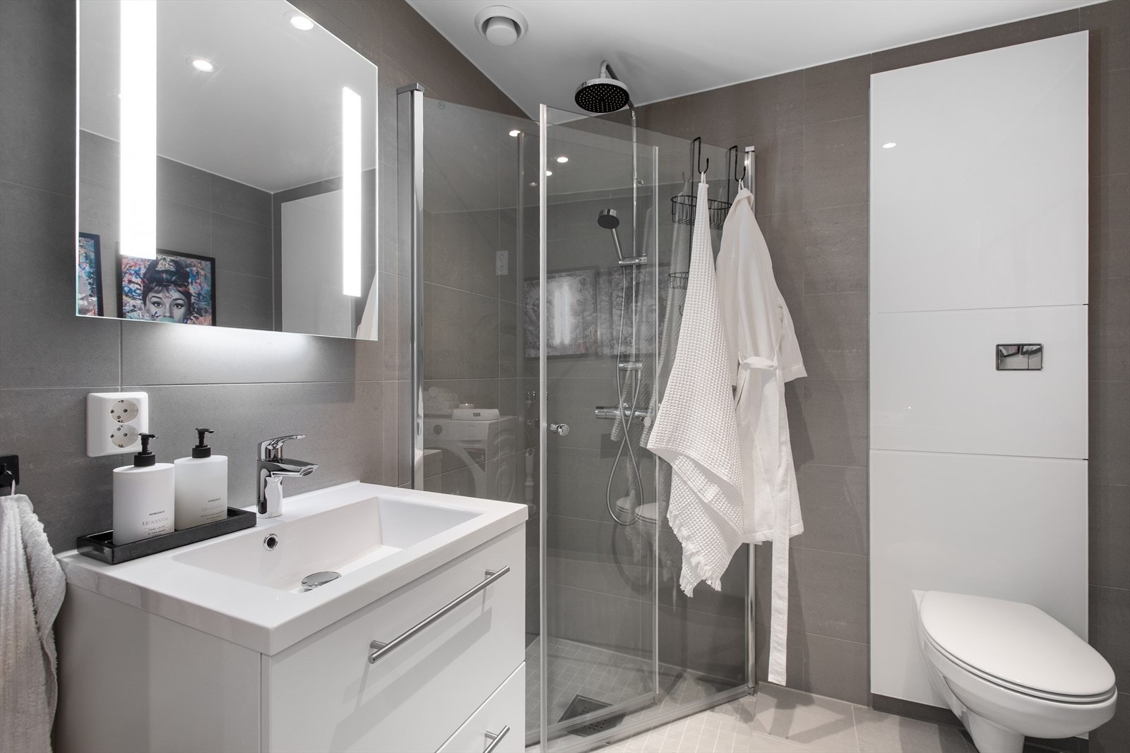 Badet er innredet med dusjhjørne med innfellbare glassvegger, vegghengt toalett og servantinnredning med skuffer som gir praktisk oppbevaringsplass. Galleribilde