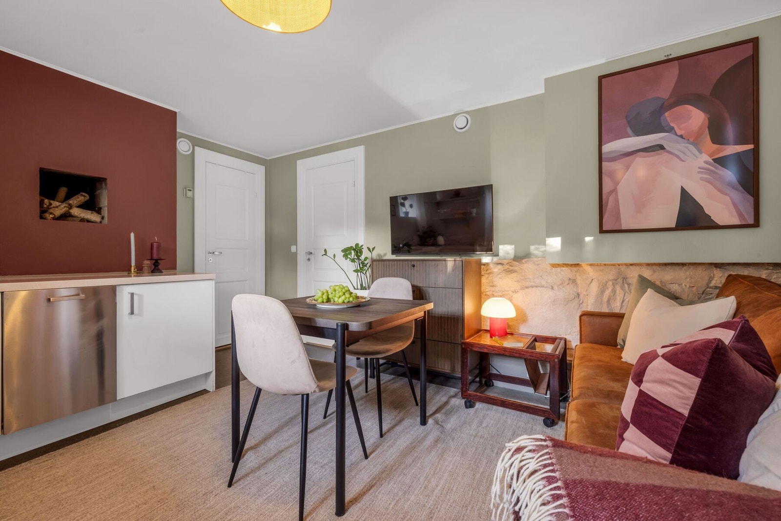 Rommet har åpen løsning til stuen med plass til sofaseksjon, lite spisebord og tv-møblement. Galleribilde