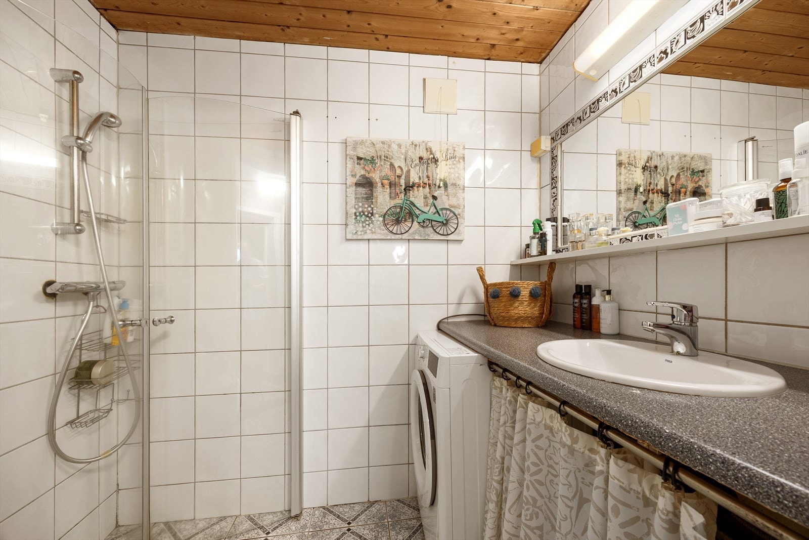 Flislagt bad innredet med benkeplate i laminat, servantskap med nedsenket servant, innmurt speil, gulvmontert klosett, dusjsone med innfelte dusjdører. Opplegg vaskemaskin. Galleribilde