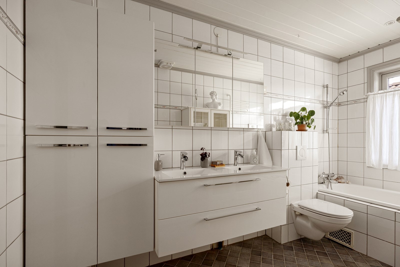 Badet i 1. etasje er innredet med etablert servantskap med dobbelt servant, veggskap med speildører og lys over, vegghengt klosett med innebygd sisterne, skap og innmurt badekar. Galleribilde
