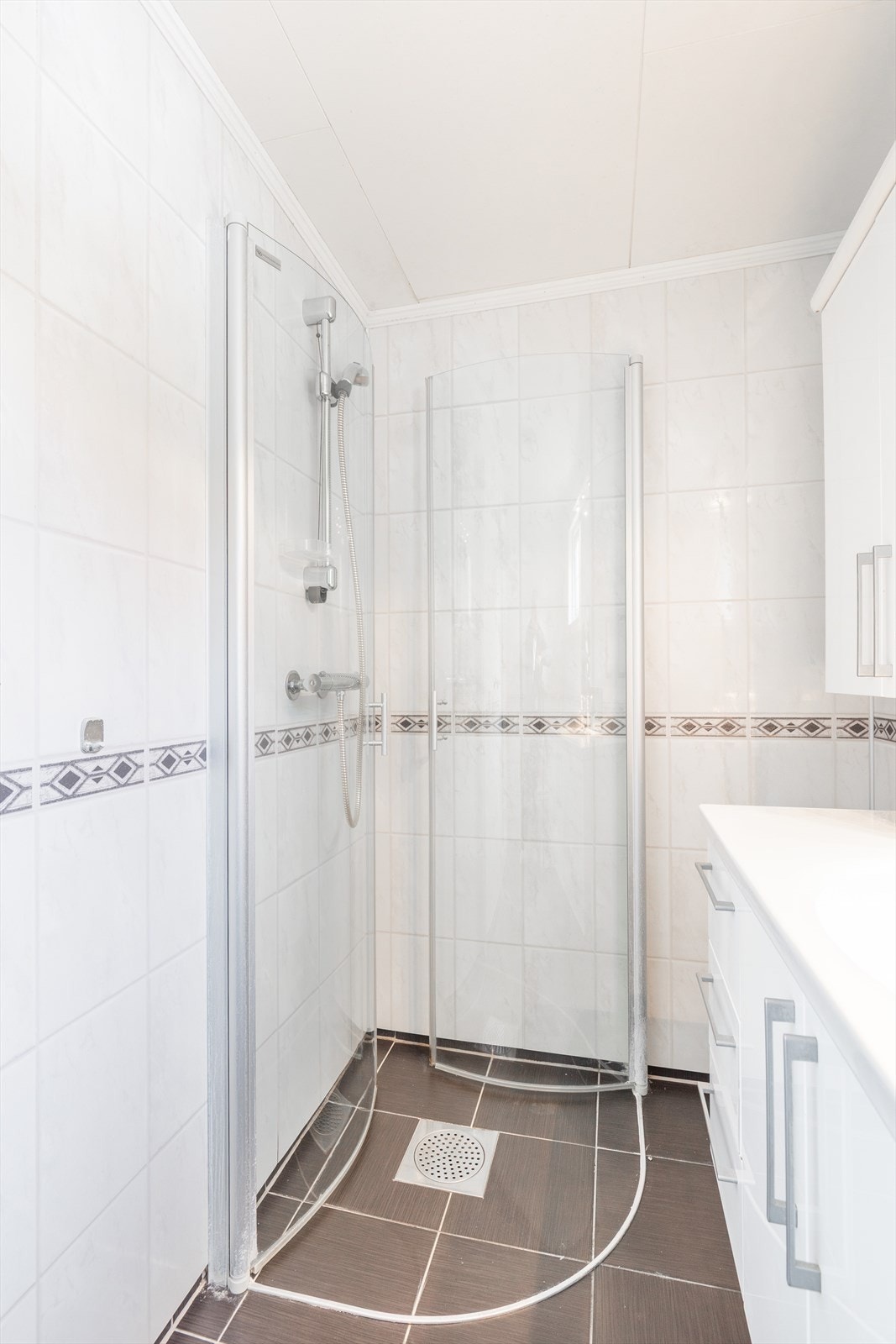 Badet er innredet med baderomsmøbel, heldekkende servant, speil med belysning, toalett og dusjhjørne med innfellbare glassdører. Galleribilde