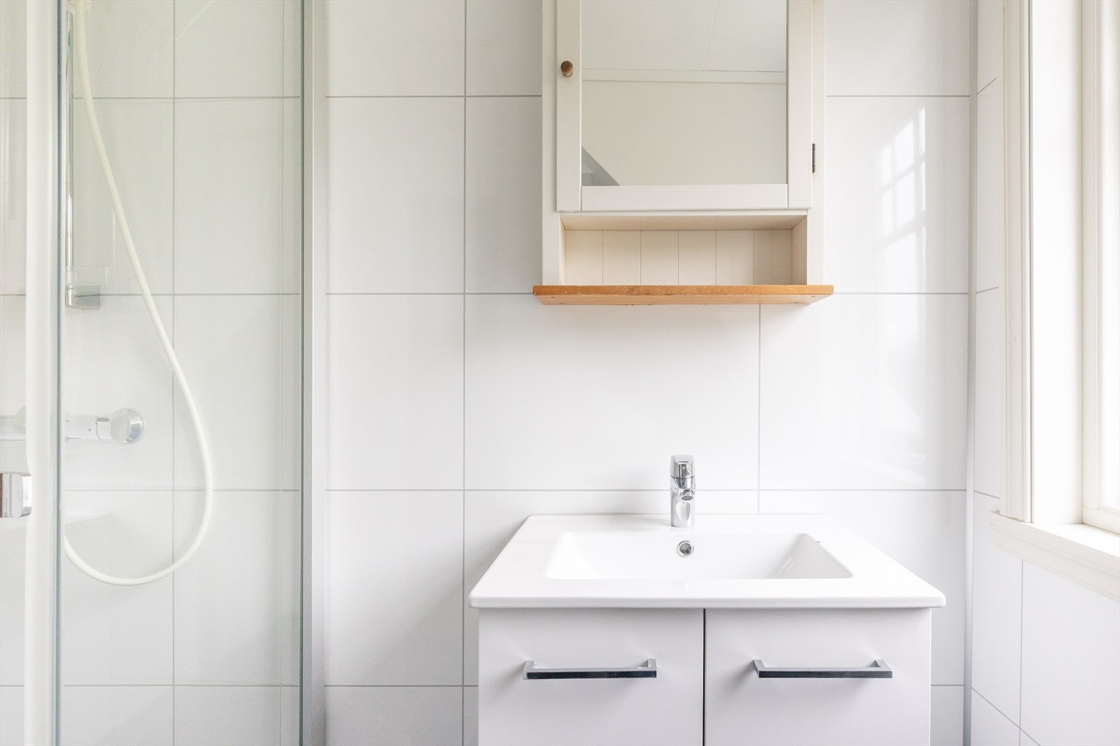 Badet er innredet med baderomsmøbel, heldekkende servant, speilskap, vegglampe, toalett og dusjhjørne. Galleribilde