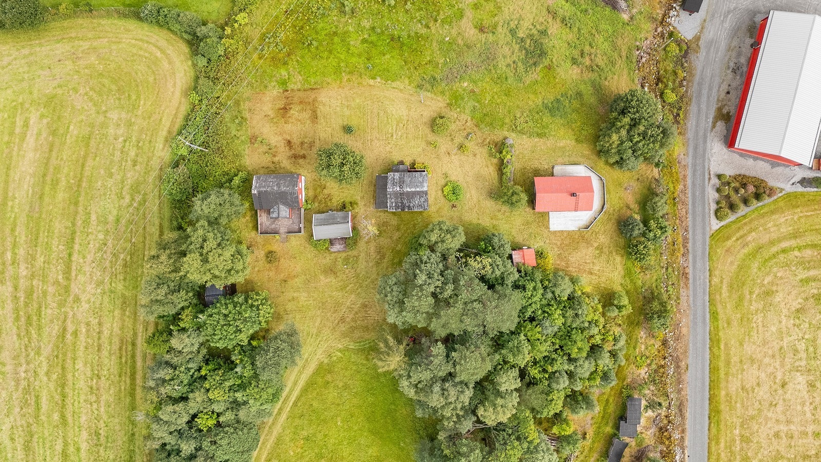 Dronebilde over nordøstre del av eiendommen. Søndre hytte til høyre, med rødt tak, opprinnelig hovedbygg i midten og nordre hytte til venstre. Galleribilde