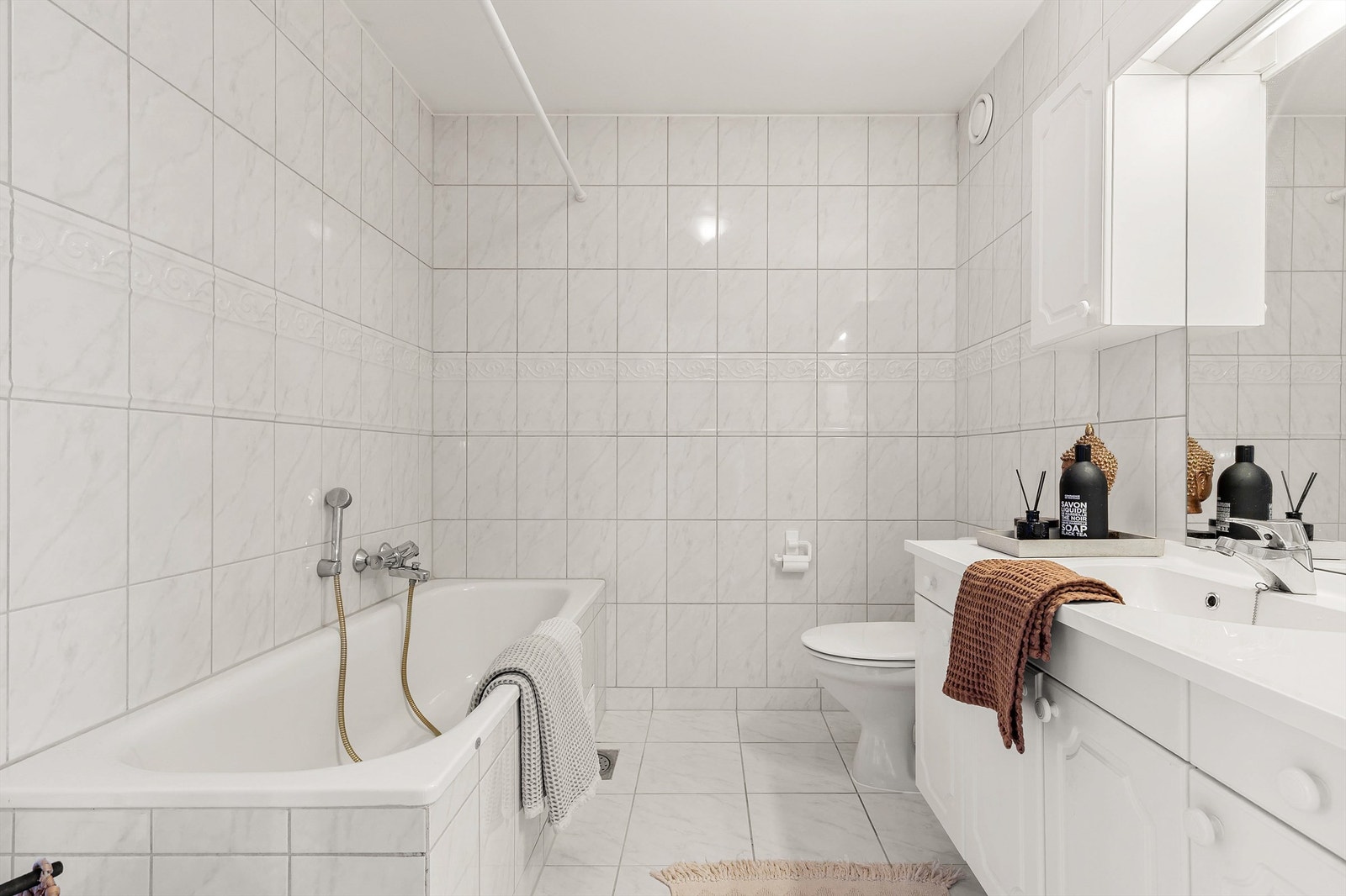 Badet har vegghengt servantinnredning med speil og overlys. Badekar med vegghengt badekararmatur og gulvstående toalett. Galleribilde