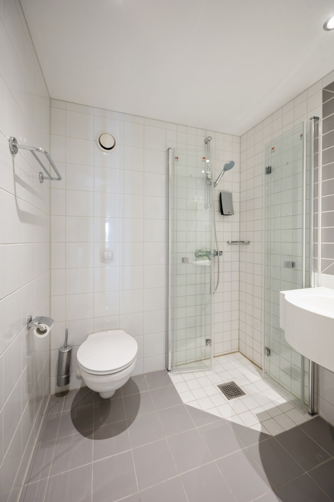 Badet har pene og tidløse fliser på vegger og gulv. Vegghengt toalett. Galleribilde