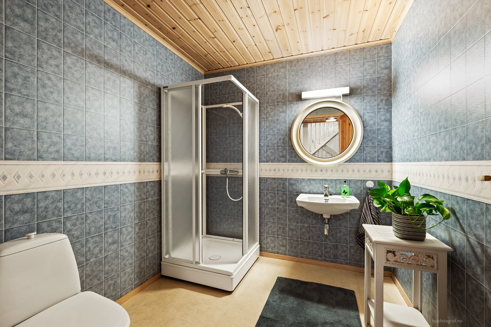 Badet er fra byggeår. Vegger med våtromstapet og himling med lasert trepanel. Gulv med vinylbelegg og elektriske varmekabler styrt via termostat. Innredet med dusjkabinett, toalett og servant med blandebatteri. Galleribilde