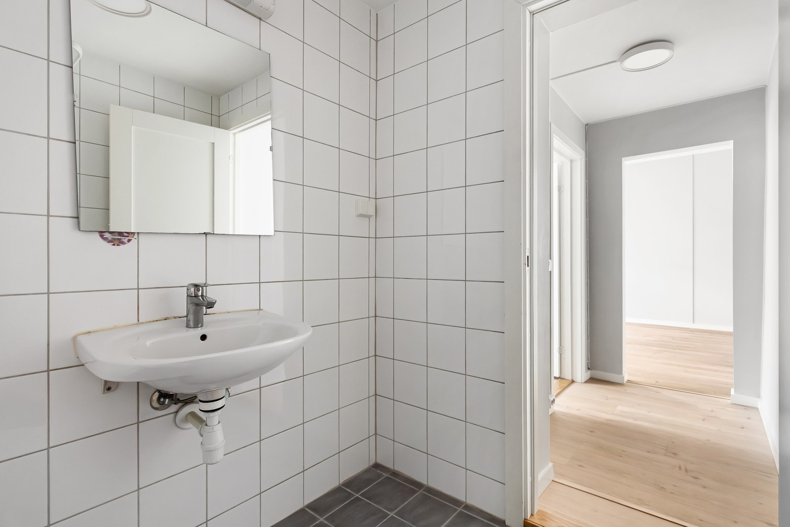 Badet er innredet med gulvmontert toalett, dusjsone med dusjforheng, servant og speil. Galleribilde