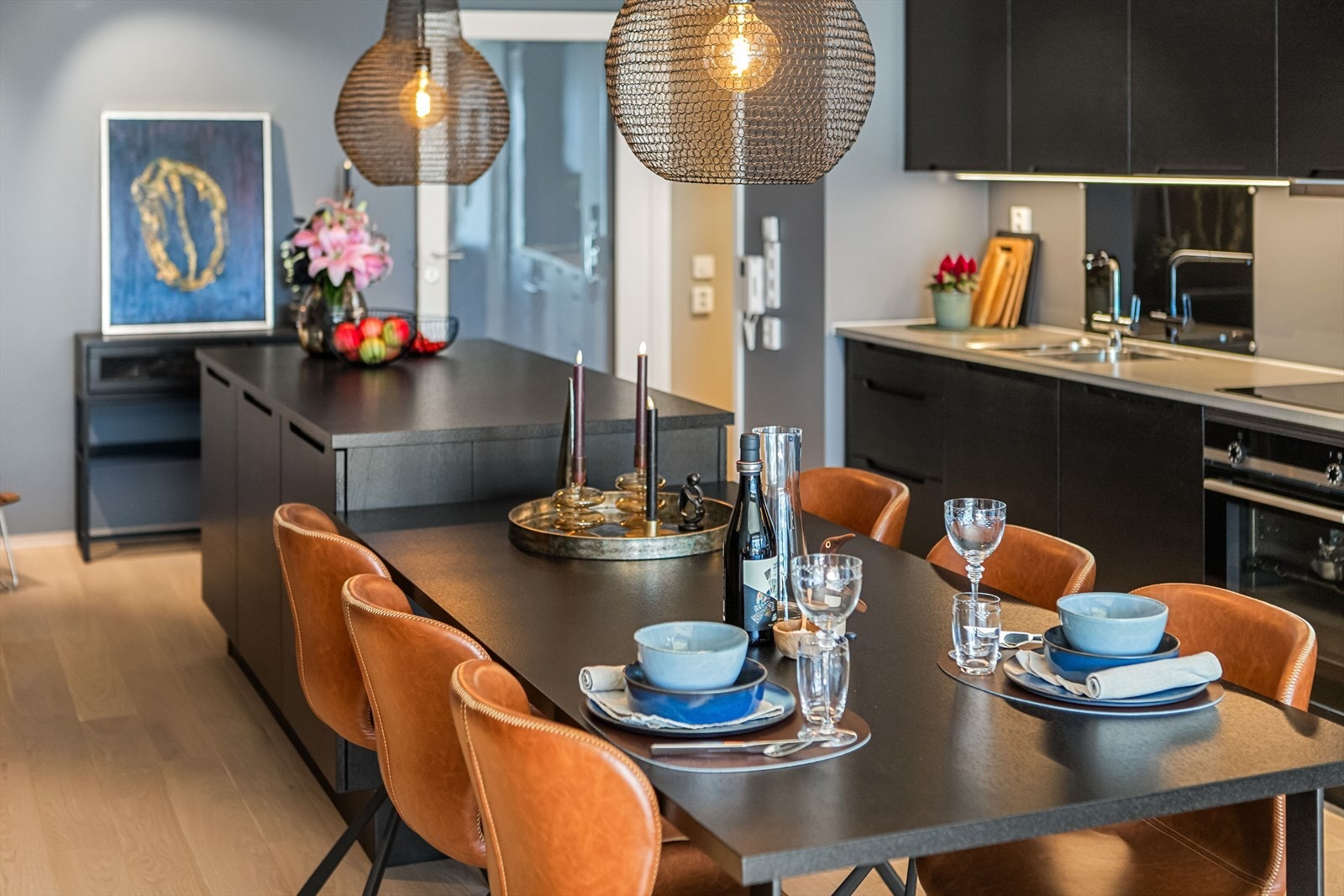 Kjøkkenet er plassert som et elegant møbel sentralt i allrommet. Innredningen har mørke, slette fronter som gir en lekker kontrast til den lyse benkeplaten. Galleribilde