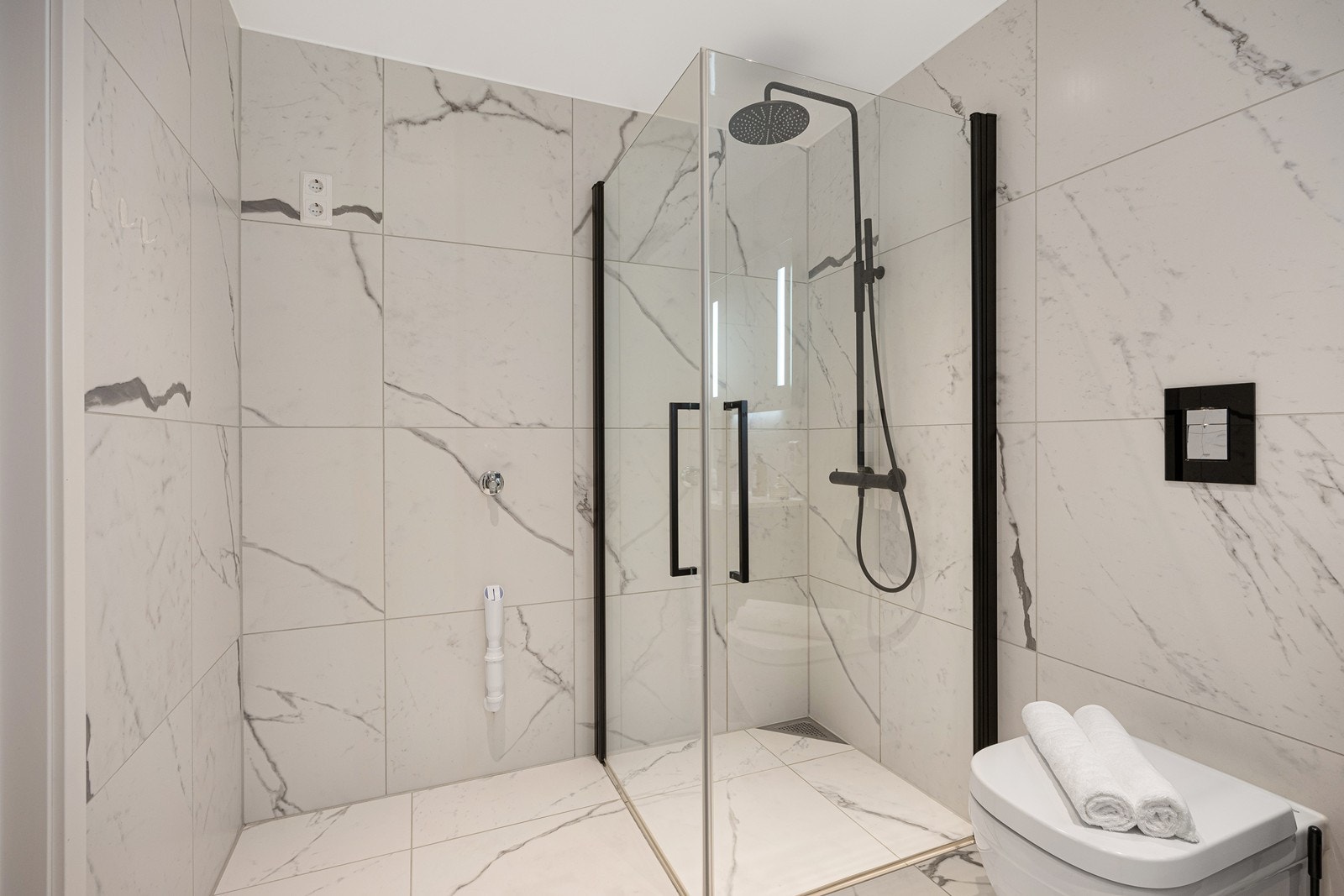 Dusjnisjen har sorte karmer og sort armatur med regnfallsdusj. Toalettet er vegghengt, og det er opplegg for vaskemaskin på badet. Galleribilde