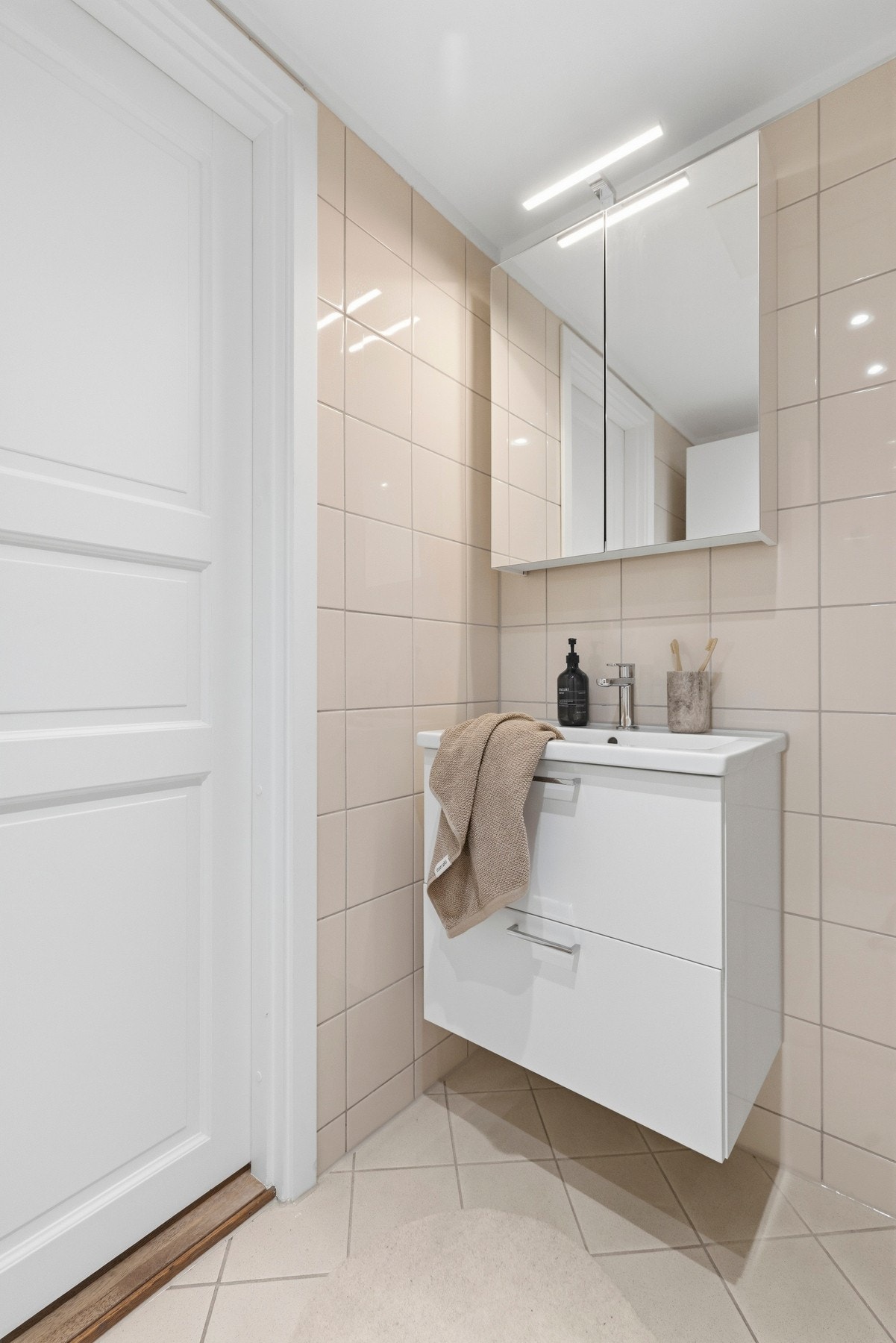 Innredningen har glatte fronter, heldekkende servant nedfelt i underskap og speilskap med belysning. Badet er videre utstyrt med vegghengt toalett og dusjhjørne. Galleribilde