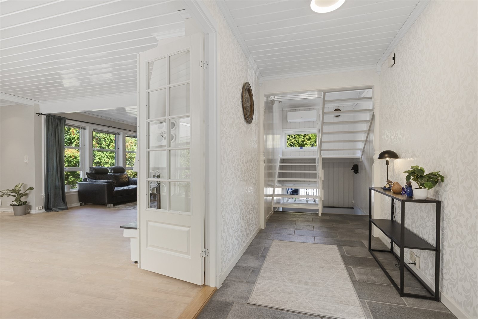 Fra hovedinngangen kommer man inn i en romslig entré med flislagt gulv. En glassdør med sprosser leder videre inn til stuen, mens trappene til loftsetasjen og underetasjen har utgangspunkt fra gangen. Galleribilde
