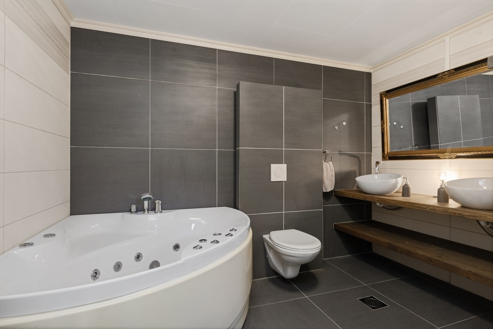 Badet i underetasjen er romslig og funksjonelt innredet med vegghengt toalett, dobbel servantinnredning med speil, dusjnisje og hjørnebadekar. Galleribilde