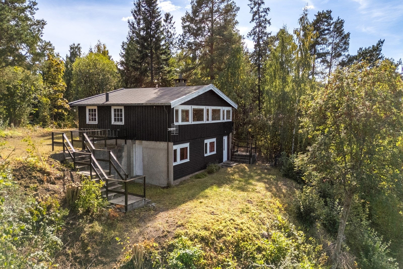 Huset ligger på en flate på toppen av et høydedrag - opp fra Taglugnveien. På husets framside skråner terrenget ned mot strand og sjø. Galleribilde