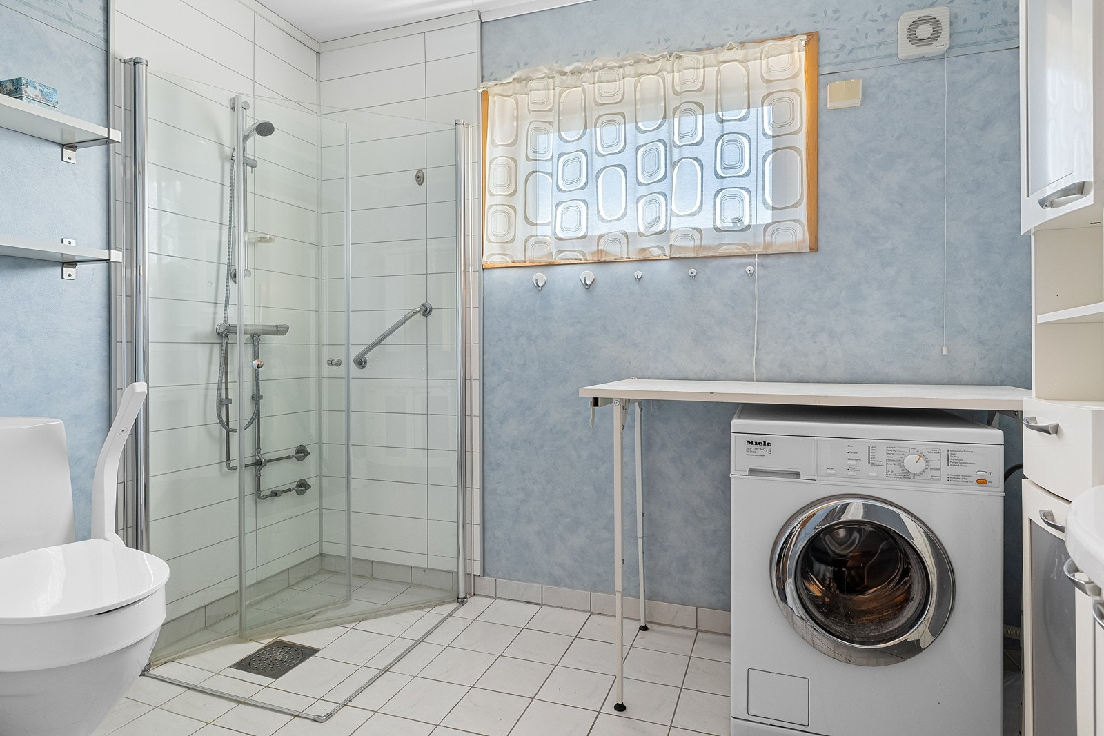 Bad/wc/vaskerom med flislagt gulv og tapetserte vegger. Dusjhjørne med glassvegger. Galleribilde