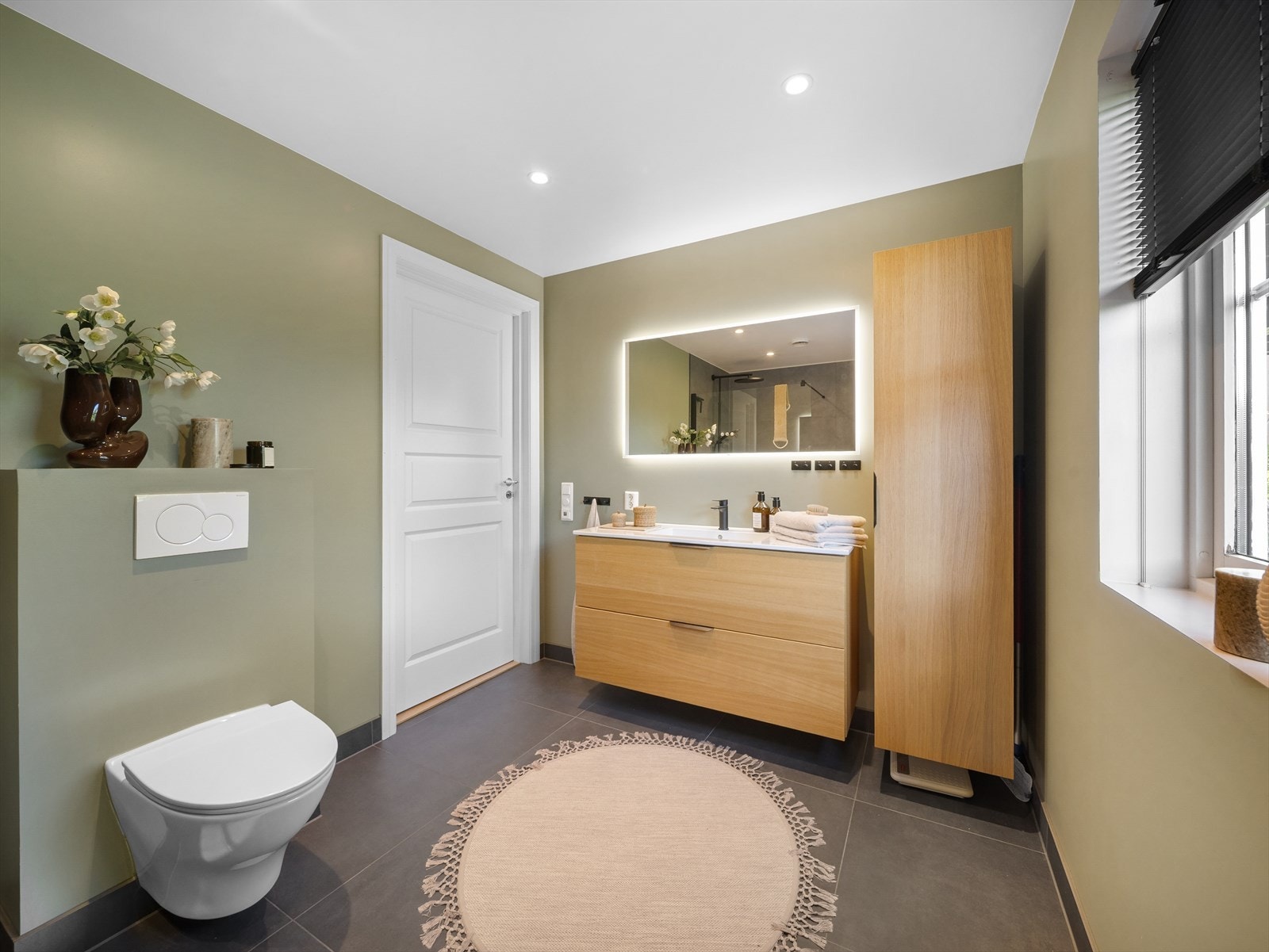 Badet er innredet med stilrene baderomsmøbler med god lagringsplass, speil med integrert belysning, dusjvegg og vegghengt toalett. Galleribilde