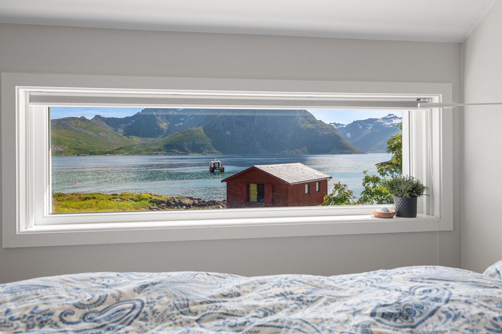 Stort soverom med horisontalt vindu og vakker utsikt mot naust og fjord