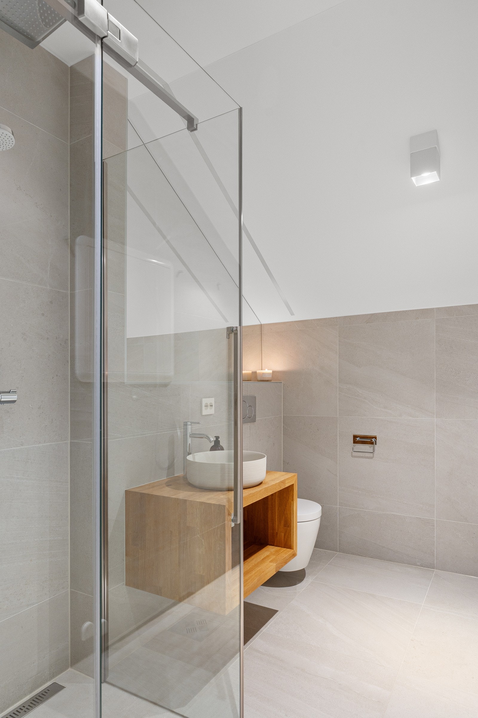 Et moderne og harmonisk bad med glassdusj, varme beige overflater og eikeinnredning som gir rommet et lunt og eksklusivt preg.
