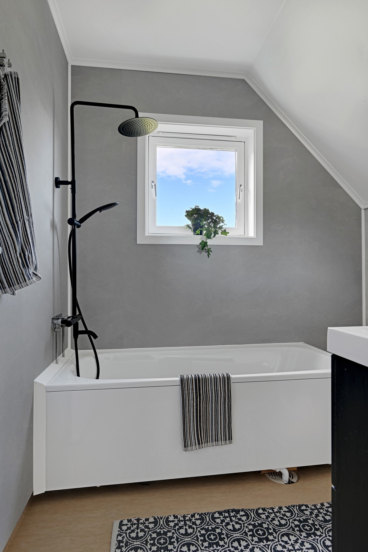 Badet har en stilren utforming med lune gråtoner, badekar med dusj og servantinnredning Galleribilde