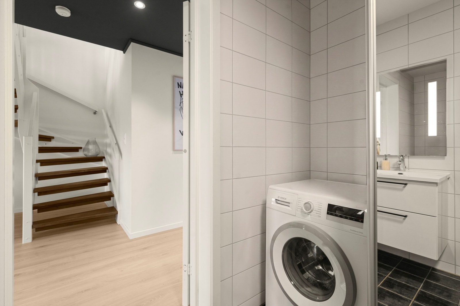 Praktisk opplegg for vaskemaskin og varmtvannsbereder er diskret plassert bak skyvedør, noe som bidrar til et ryddig og helhetlig uttrykk på badet. Galleribilde