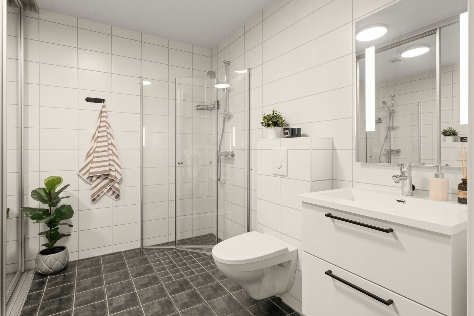 Badet i 1. etasje har et lyst og tidløst uttrykk med flislagte vegger og mørkere fliser på gulv. Den romslige utformingen gir god bevegelsesfrihet og en behagelig romfølelse. Galleribilde