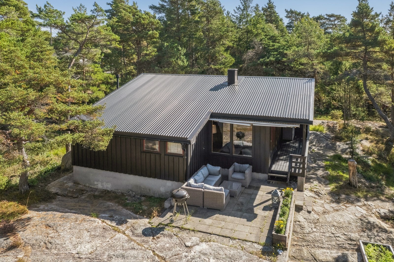 Hytta ligger fint plassert på naturtomten og har en hyggelig uteplass som innbyr til rolige dager i solen. Den mørke fasaden gir et klassisk og tidløst uttrykk. Galleribilde