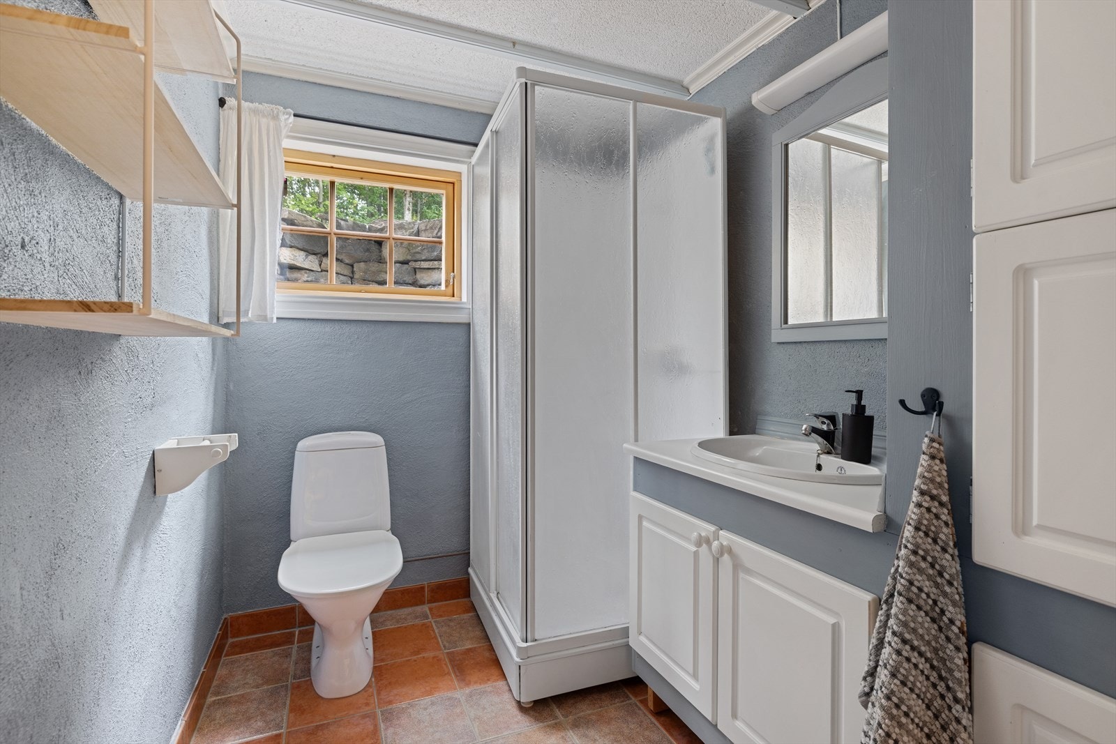 Bad i underetasjen med malte murvegger og flislagt gulv med varmekabler. Badet har gulvmontert toalett og dusjkabinett. Galleribilde