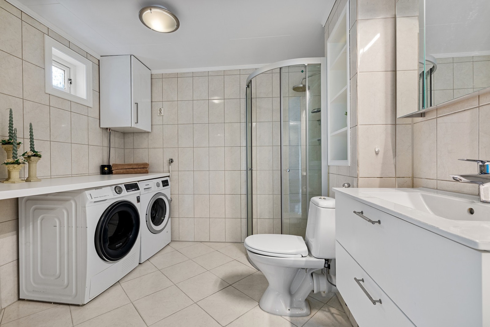 Badet er flislagt og har gulvvarme. Det er innredet med servantinnredning, speilskap, gulvmontert toalett og dusjhjørne med regnfallsdusj. Galleribilde