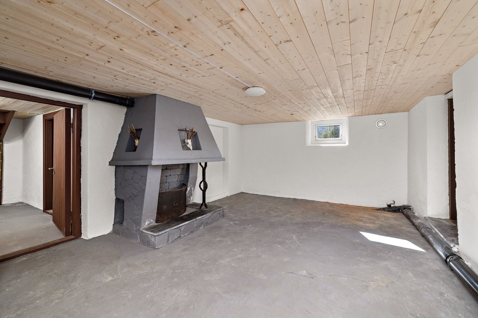 Kjellerrom med peis med åpen grue og dør med utgang til terreng. Galleribilde