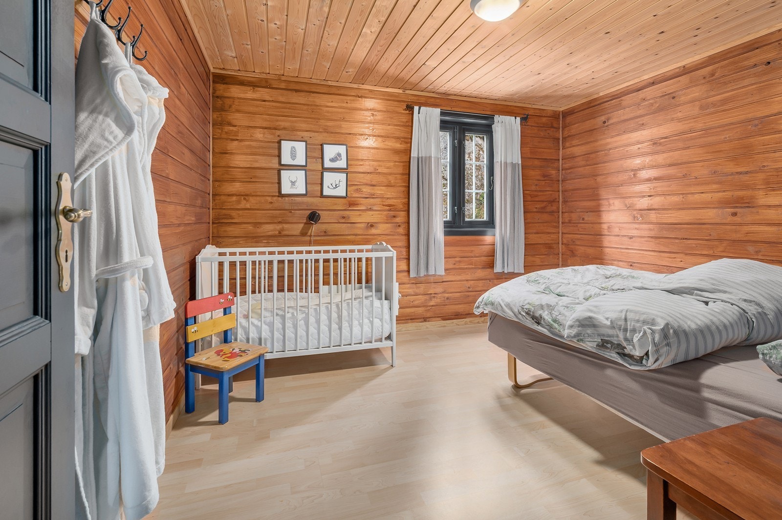 Et av de to soverommene i første etasje har plass til både dobbeltseng og barneseng, og fungerer som et praktisk og fleksibelt familierom. Galleribilde