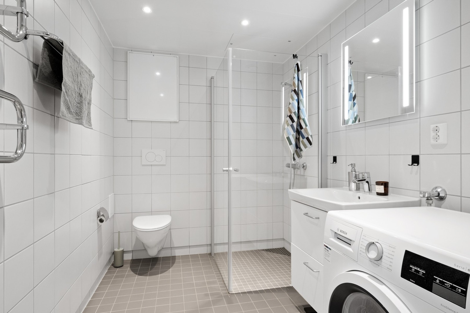 Badet er levert som en komplett baderomsmodul med flis på vegg og gulv, og har dusjhjørne med glassvegger. Galleribilde