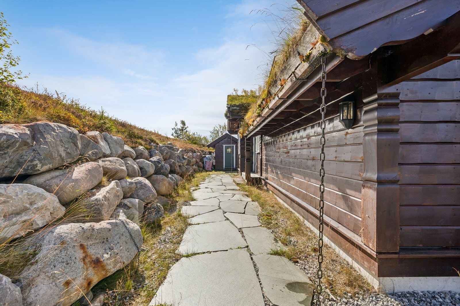 Forstøtningsmur i naturstein og hellelagt gangsti langs hytta. Galleribilde