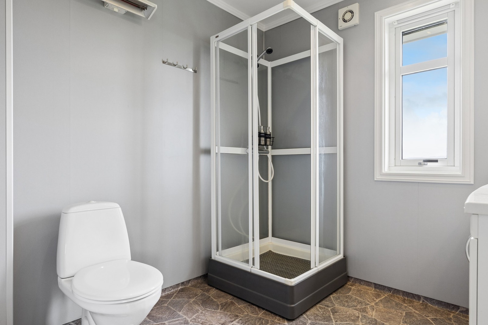Badet er utstyrt med dusjkabinett, toalett og har baderomsplater på veggene. Galleribilde