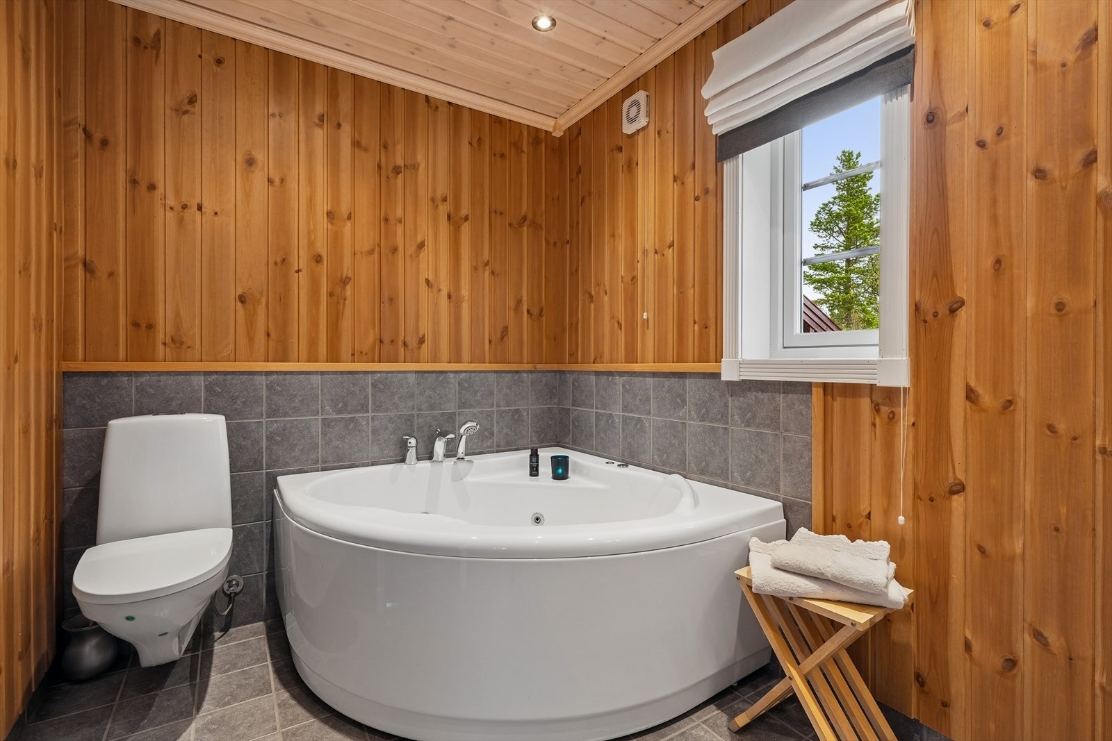 Badet er innredet med servantskap og frittstående servant, speil med belysning, vegghengt toalett, hjørnebadekar og dusjhjørne med dusjvegger. Galleribilde