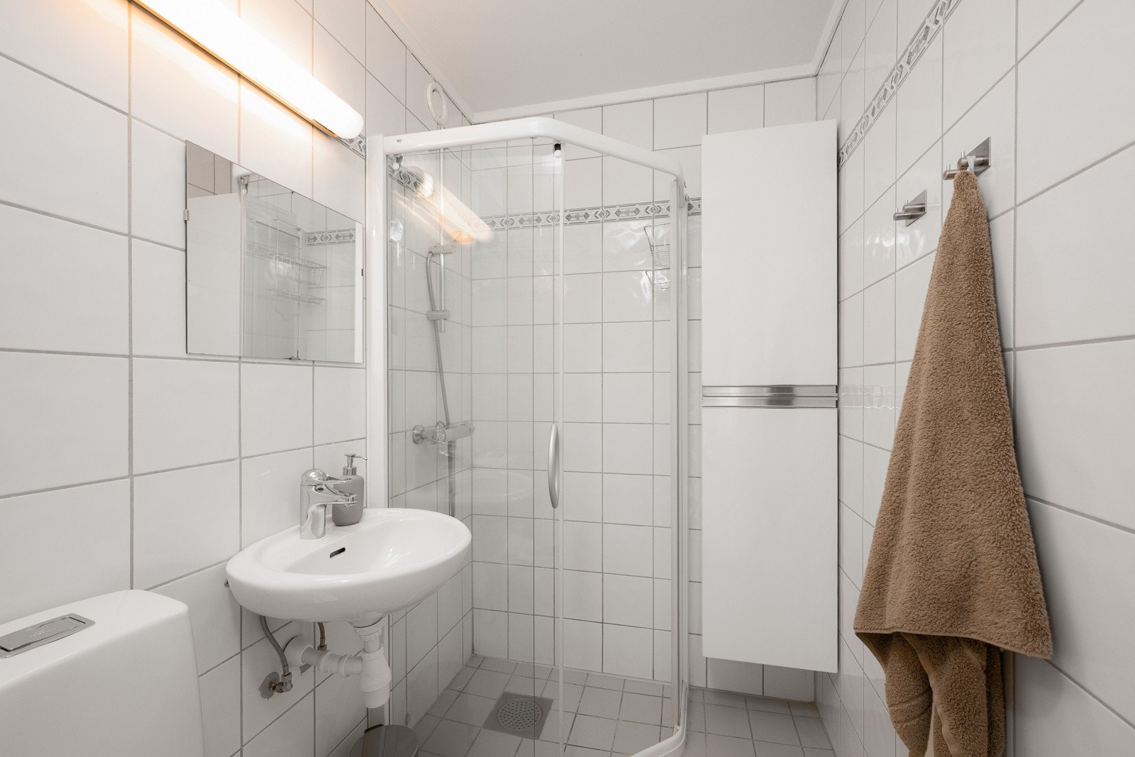 Baderom innredet med fliser på vegger og gulv, servant, speil og dusjvegger. Galleribilde