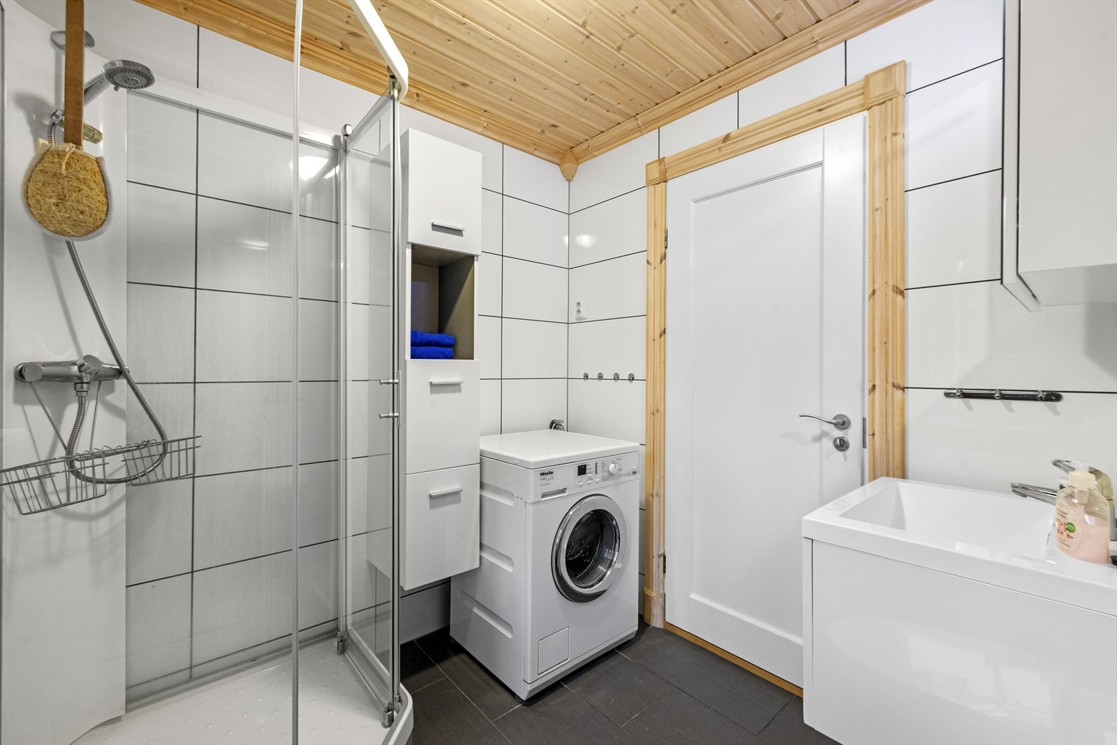 Badet er utstyrt med servant over skuffeinnredning, speilskap med belysning, vegghengt toalett, dusjkabinett og opplegg til vaskemaskin Galleribilde